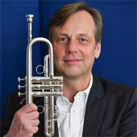 Dieses Bild zeigt Christian Haag. Er ist fortgeschrittenen Alters, sein Haar ist grau. Er spielt Trompete in der HSD Big Band.